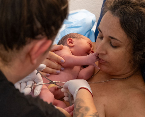 A mom with her newborn baby and her midwife is cutting the nuchal cord.