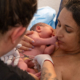 A mom with her newborn baby and her midwife is cutting the nuchal cord.