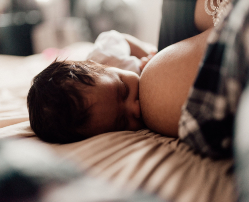A newborn who is sidelying breastfeeding and a new mother resting with support from a sleep coach.